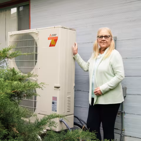 A woman leaning on a heat pump outside her home